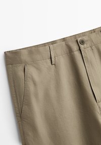 Beige katoenen broeken met een rechte voorkant, twee zijzakken en een knoopsluiting. De stof heeft een gladde textuur en een subtiele diagonale weving.