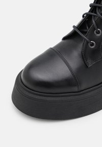 Stivale in pelle nera con punta rotonda, cucitura rinforzata e suola in gomma piatta. Presenta un design con lacci e occhielli metallici per una chiusura sicura.