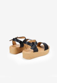 Black leather platform sandals with crisscross straps, cork sole, and buckle detail. Smooth texture with a slightly raised heel.