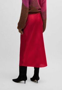 Red satin midi skirt with a smooth texture, featuring a side slit and paired with black knee-high boots. The outfit is completed by a colorful knit sweater.