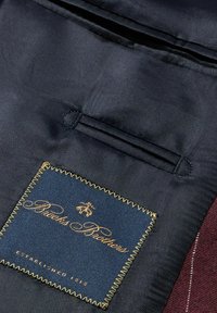 Námořnická textilie interiéru s burgundským akcentem. Obsahuje modrou nášivku se zlatým prošíváním a textem "Brooks Brothers", založeno 1818.