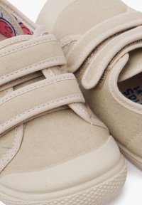 Scarpe in tela beige con due cinturini regolabili a strappo, punta arrotondata, suola in gomma testurizzata e fodera interna a fantasia.