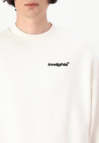 White sweatshirt featuring a ribbed crew neck and a small black embroidered logo that reads "lowlights®" on the upper left chest.