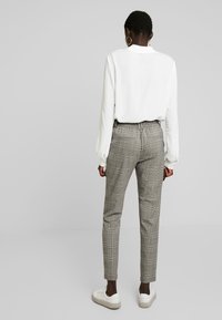 Vit långärmad blus, grå rutiga byxor med elastisk midja och vita sneakers med texturerade sulor.