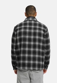 Sorthvidternetternet flannel skjorte med lange ærmer, der har en klassisk krave og knapdetaljer, vist fra ryggen.