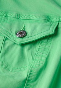 Tissu vert vif avec une texture lisse, comportant un bouton en métal et des détails de couture sur la zone de la poche.