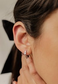 Orecchino a cerchio in argento con una pietra preziosa trasparente ben evidente, arricchito da dettagli scintillanti più piccoli, che mette in risalto una finitura lucida e una texture liscia.