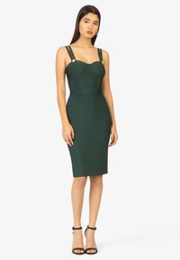 Grünes, tailliertes Kleid mit gerippten Details am Oberteil, verstellbaren Trägern und goldenen Akzenten. Der Saum reicht bis unter das Knie.