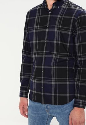 Man wearing a long-sleeve dark navy and black plaid button-up shirt with light grey lines, paired with light blue jeans.