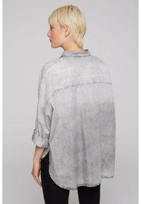 Gray denim shirt with a slightly faded design. Features rolled sleeves and white text on the back stating motivational phrases.