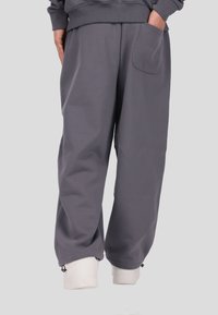 Szare spodnie dresowe wykonane z miękkiego materiału, charakteryzujące się luźnym krojem, elastycznym pasem, boczną kieszenią oraz regulowanymi ściągaczami przy kostkach.