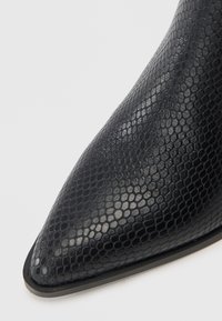 Botine negre din material sintetic cu imprimeu de șarpe, cu vârf ascutit și textură netedă. Prezintă o talpă subțire neagră cu detalii minimaliste.