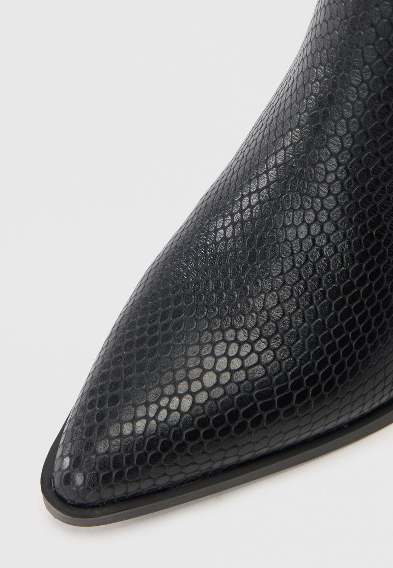 Czarny, sztuczny botek z motywem węża, z wąskim noskiem i gładką teksturą. Posiada cienką czarną podeszwę z minimalistycznym wykończeniem.