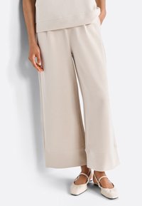 Pantaloni a gamba larga beige realizzati in tessuto morbido, con una superficie liscia, vestibilità rilassata e dettagli di cucitura discreti all'orlo.