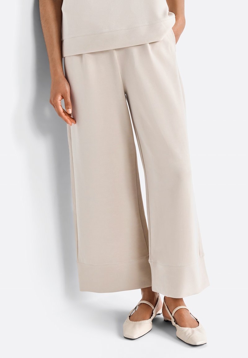 Pantaloni a gamba larga beige realizzati in tessuto morbido, con una superficie liscia, vestibilità rilassata e dettagli di cucitura discreti all'orlo.