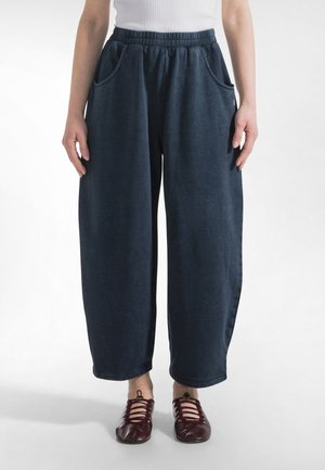 Osoba ubrana w luźne, ciemnoniebieskie spodnie z elastycznym paskiem w talii i bocznymi kieszeniami oraz czerwone, sznurowane buty na płaskim obcasie na białym tle.