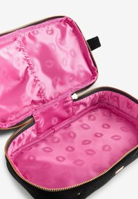 Borsa cosmetica nera con chiusura a zip, con interno in satin rosa decorato con labbra. Esterno liscio con dettagli in oro.