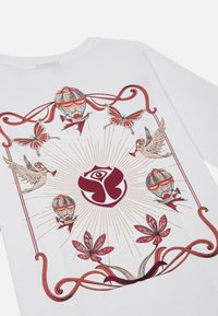 Witte t-shirt met kleurrijke bedrukte ontwerpen van vlinders, vogels, luchtballonnen en een centraal logo, omkaderd door rode zwirls.