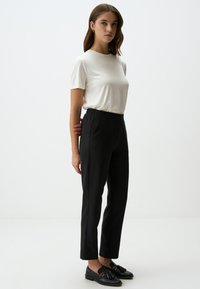 T-shirt bianca a maniche corte abbinata a pantaloni neri con righe sottili. I pantaloni presentano una vita elastica e tasche laterali discrete. Mocassini neri.