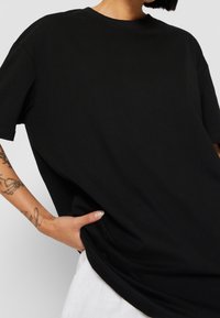 Černé bavlněné tričko s volným střihem, krátkými rukávy a kulatým výstřihem. Hladká textura a lemované okraje. Žádné viditelné vzory či grafika.