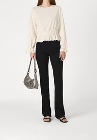 Krémová halenka s dlouhými rukávy a nařaseným pasem, kombinovaná s černými rozšířenými džínami a stříbrnou kabelkou. Černé sandály doplňují vzhled.