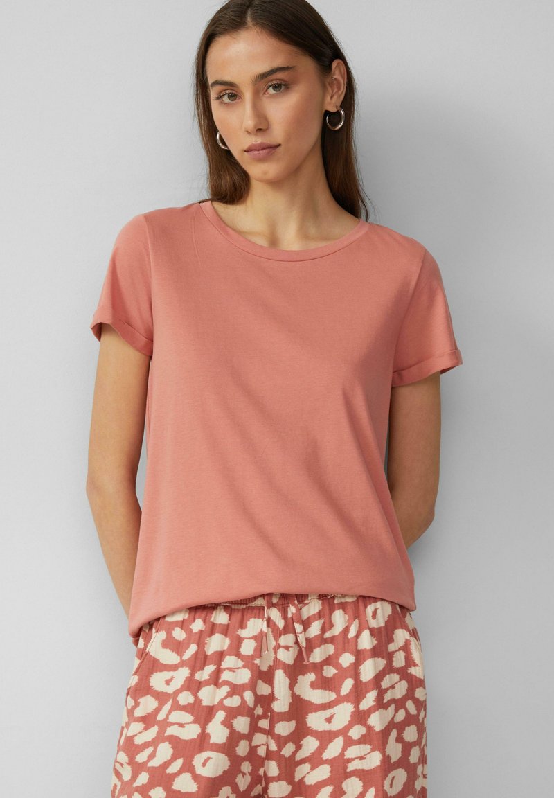 Rosa Kurzarm-T-Shirt aus weichem Stoff mit Rundhalsausschnitt, kombiniert mit lockeren Hosen mit Muster, die ein helles abstraktes Design aufweisen.