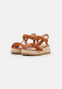 Brown suede wedge sandals with ankle straps, knotted front detail, and woven espadrille-style platform soles on a white background.