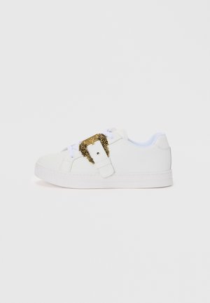Hvite sneakers med en jevn tekstur, med en dekorativ gullspenne og merkevaredetalj på siden; flat såle og snøring.