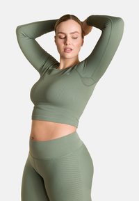 Olivgrünes, geripptes Sport-Crop-Top mit langen Ärmeln, kombiniert mit passenden, hochgeschnittenen Leggings, die ein seitliches Texturmuster aufweisen.