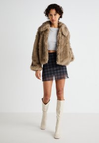 Faux fur brun jakke, lys grå crop top, rutete mini skjørt, og beige knehøye støvler. Myk tekstur med en avslappet passform og crop design.