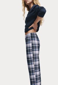 Marineblauw langemouwen shirt gecombineerd met geblokte pyjamabroek in blauw, wit en grijs. De broek heeft een elastische tailleband en een relaxte pasvorm.