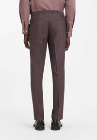 Dunkelbraune, maßgeschneiderte Hose mit dezentem Karo-Muster, schmal zulaufender Passform, Gesäßtaschen und kombiniert mit schwarzen Business-Schuhen.