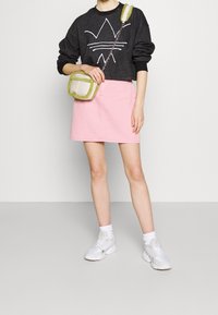 Svart sweatshirt med vitt grafiskt mönster, kombinerad med en rosa denimkjol. En liten grön och vit crossbody-väska fulländar outfiten.