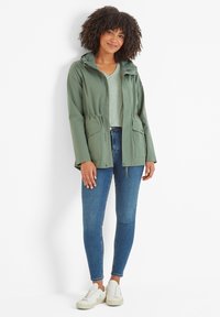 Green hooded jacket with a drawstring waist, two front pockets, paired with a light green top, blue jeans, and white sneakers.