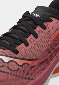 Κοντινή λήψη κόκκινου και μαύρου αθλητικού παπουτσιού με μαύρα κορδόνια, υφασμένο επάνω μέρος με υφή και λεπτομέρειες της μάρκας στο πλάι και στη γλώσσα του παπουτσιού.