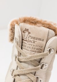 Bottine en daim beige avec un col en fausse fourrure, lacets ronds, œillets en métal et une étiquette de marque embossée avec "Panama Jack, Fabriqué en Espagne."