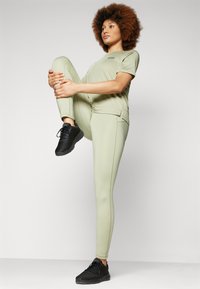 Set atletico verde chiaro con top a maniche corte e leggings aderenti, abbinato a sneakers nere. Materiale morbido con una texture liscia.