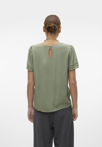 Grøn kortærmet bluse med rund halsudskæring og en keyhole-detail bagpå. Glat stof, let løs pasform, lagdelt ærmedesign.