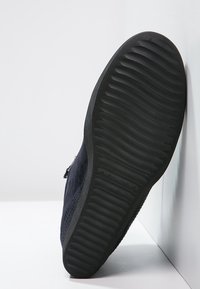 Chaussure en suède marine avec un dessus texturé et une semelle en caoutchouc noir, dotée d'un motif nervuré pour une meilleure adhérence et un soutien.