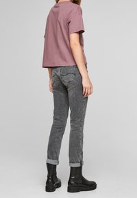 Krátký rukáv, zkrácený tričko v barvě mauve spárované s vysokým pasem šedými džíny. Černé kotníkové boty s texturovaným povrchem dotvářejí vzhled.