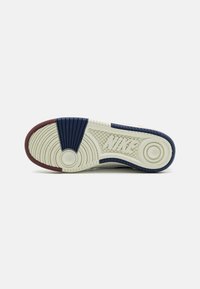 Nike sneaker sole with a textured design. Features navy blue, maroon, and off-white rubber elements. Logos and circular patterns included.