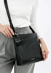 Black leather handbag with a textured finish, featuring a detachable heart-shaped keychain. Adjustable strap, compact design, silver hardware.