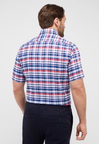 Camicetta a maniche corte a scacchi con un motivo a quadri rosso, blu e bianco, con colletto classico e tessuto di cotone. Viene indossato un pantalone corto scuro.