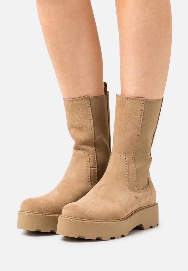 Tan ankle boots made of suede feature a chunky platform sole with a textured finish and exposed stitching on the upper.
