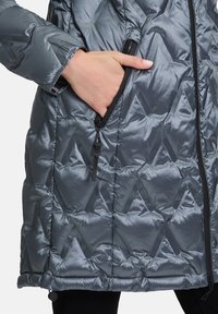 Grijze pufferjas met een diamanten quiltpatroon, ritssluitingen aan de zijkant en zwarte accenten. Gladde, glanzende stof met een getailleerde pasvorm.