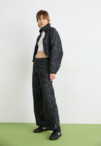 Jaqueta cropped preta com padrão floral, combinada com calças largas a condizer, ambas com um acabamento texturizado. Ténis pretos completam o visual.
