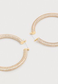 Náušnice kruhového tvaru zo zlata s jemne zakriveným dizajnom, zdobené priehľadnými kryštálmi na prednej strane. Bezpečné zapínanie na kolík, ľahká konštrukcia.