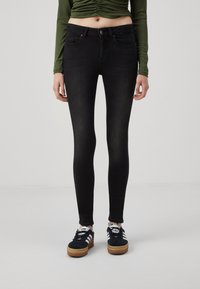Crne skinny traperice s visokim strukom, s prednjim džepovima, suptilnim izblješnjem i kombinirane s crnim tenisicama.