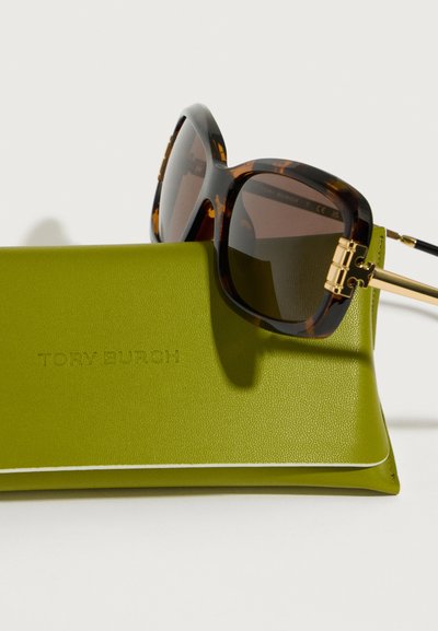 Csempés négyzet alakú napszemüveg barna lencsékkel, zöld műbőr tokkal, amelyen a "TORY BURCH" felirat látható, fehér díszítéssel.