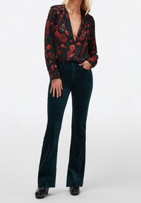 Zwarte bloemenblouse met rode bloemen, diepe V-hals, lange mouwen, gecombineerd met donkerblauwe flared corduroy broek en zwarte klompen.